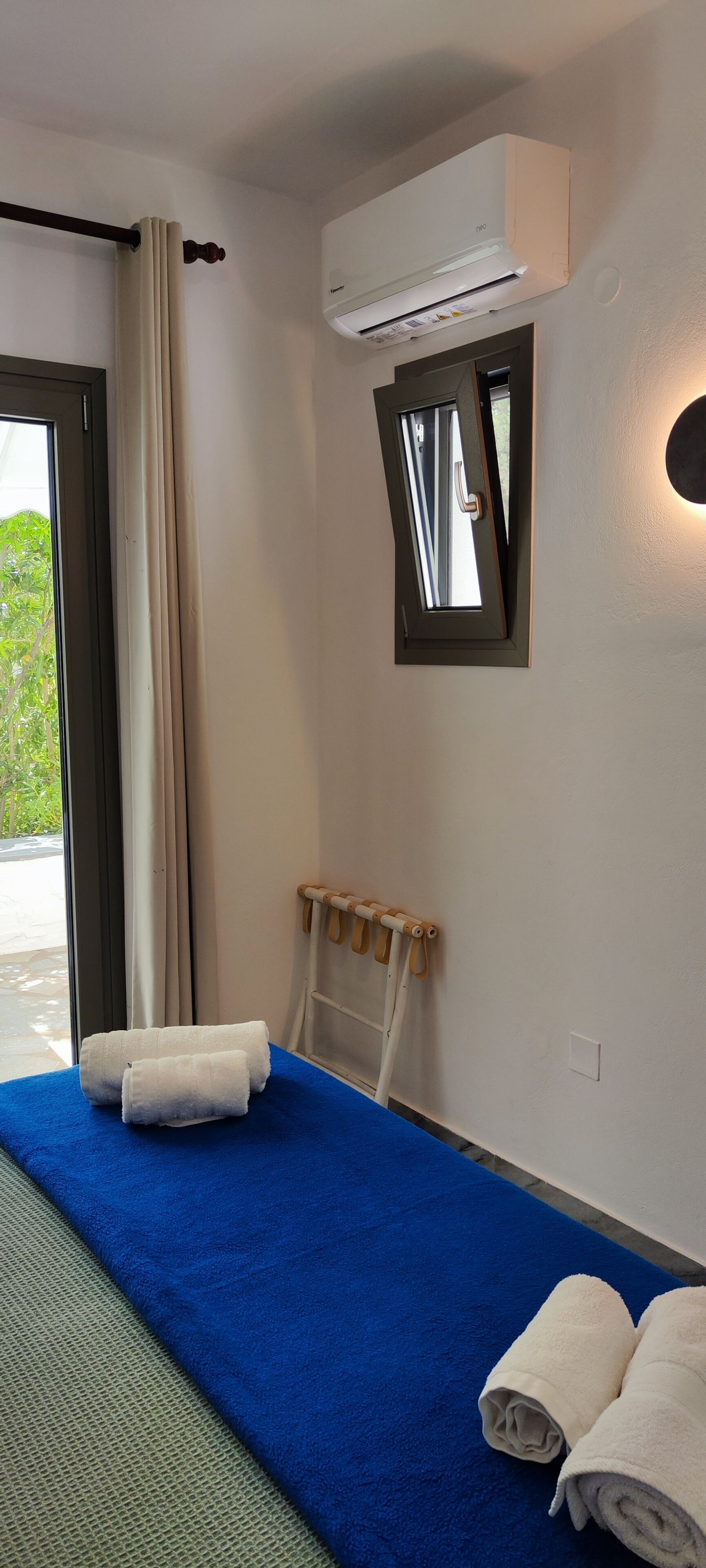 Una habitación de hotel con una cama, una ventana con cortinas, un equipo de aire acondicionado y un perchero para toallas.