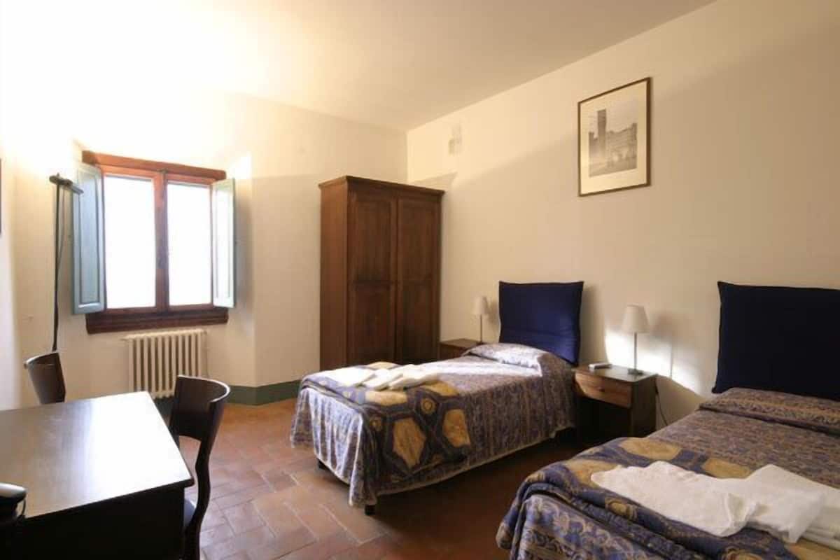 Una habitación con dos camas, un armario de madera, una mesa y una ventana con persianas.