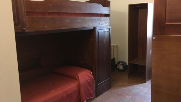 Un letto a castello con testiera in legno, una piccola credenza e un termosifone nell'angolo.