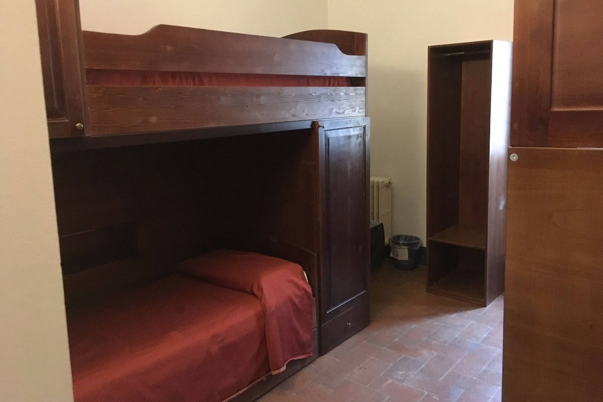 Una cama litera con cabecera de madera, un armario pequeño y un radiador en la esquina.