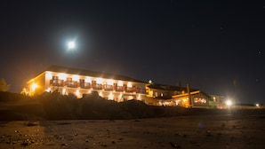 Um edifício com várias varandas e um grande letreiro iluminado, localizado em uma área arenosa com vista desobstruída para o céu noturno.