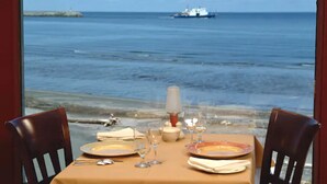 Mesa posta para dois com vista para o mar e um barco ao longe.