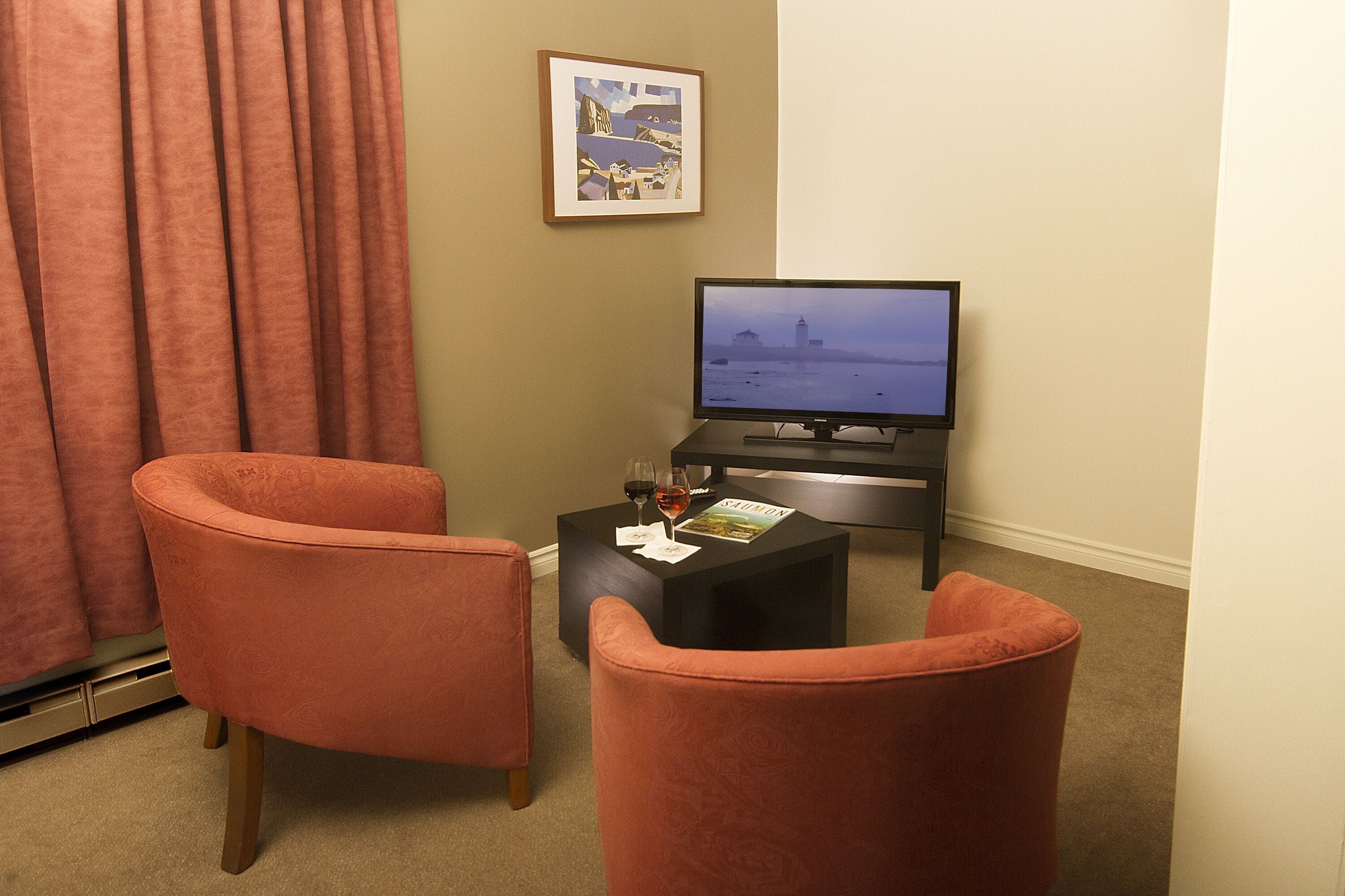 A living room with two orange chairs, a black coffee table with a magazine, and a television displaying a cityscape.