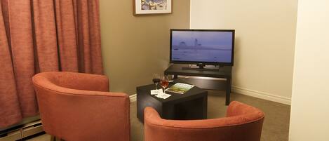 A living room with two orange chairs, a black coffee table with a magazine, and a television displaying a cityscape.
