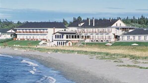 Um imóvel à beira-mar com vários edifícios, uma praia de areia e ondas chegando à costa.