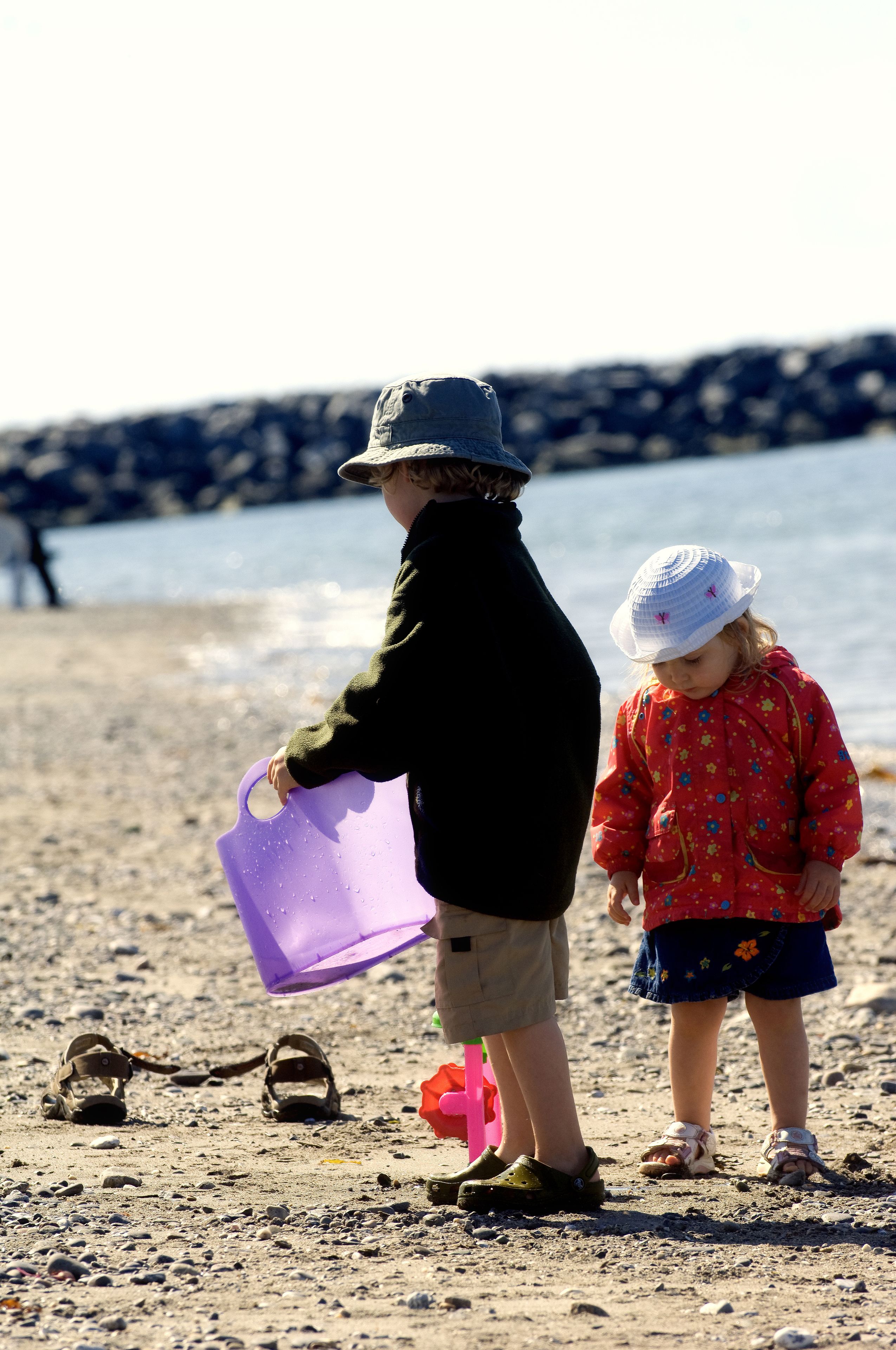 Two children playing on a sandy beach with a rocky shoreline in the background.