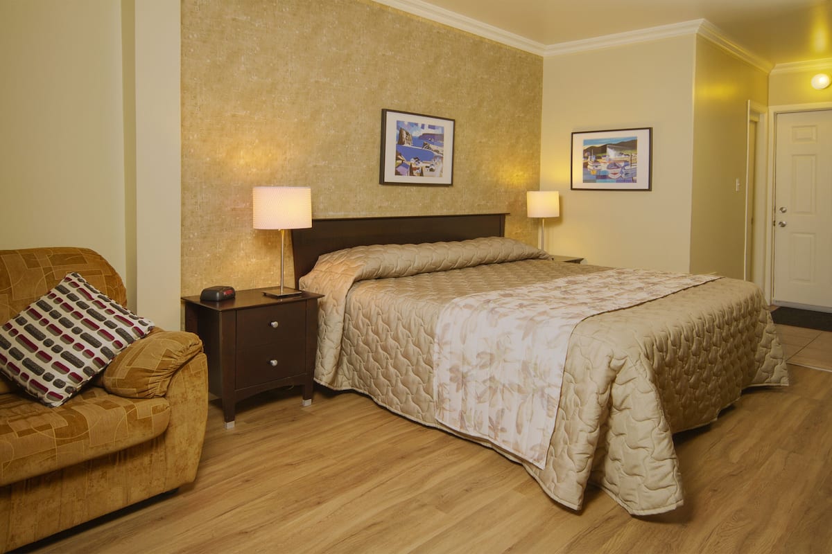 Ein Hotelzimmer mit Bett, Nachttisch, Lampe, Stuhl und zwei gerahmten Bildern an der Wand.