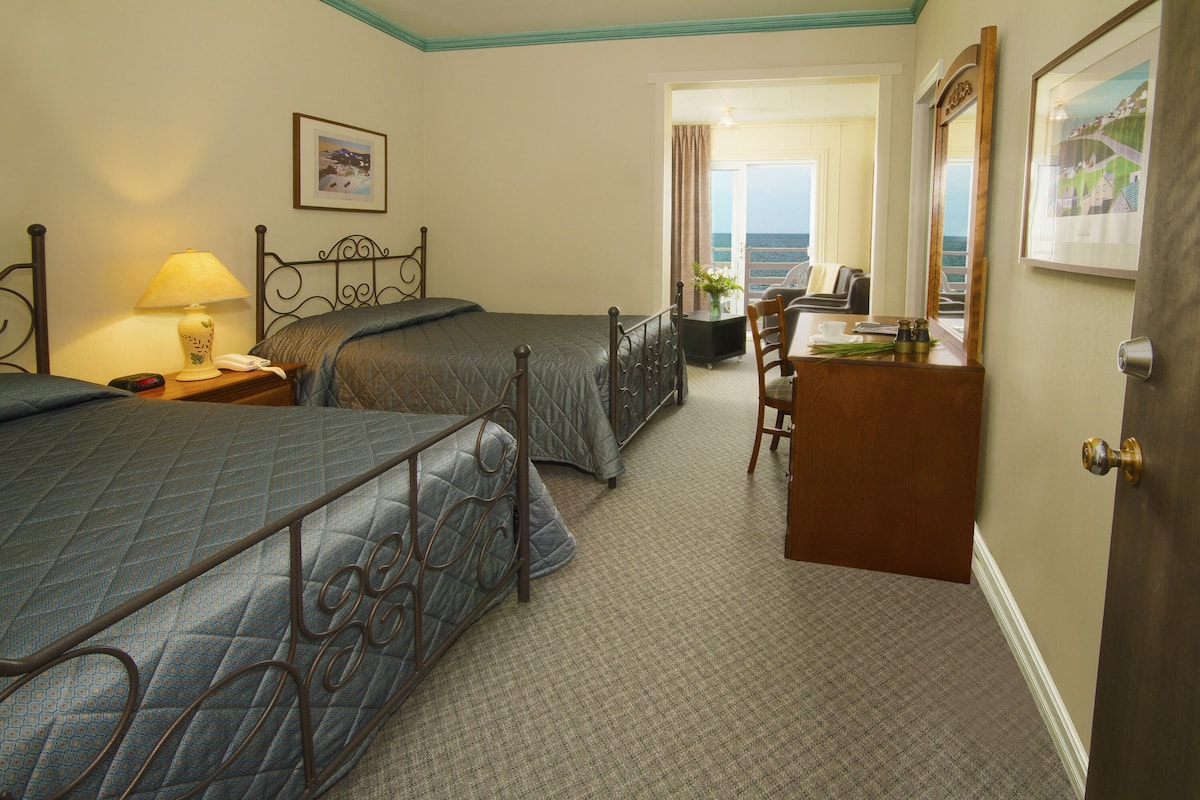 Ein Hotelzimmer mit zwei Betten, einem Schreibtisch und Blick aufs Meer.