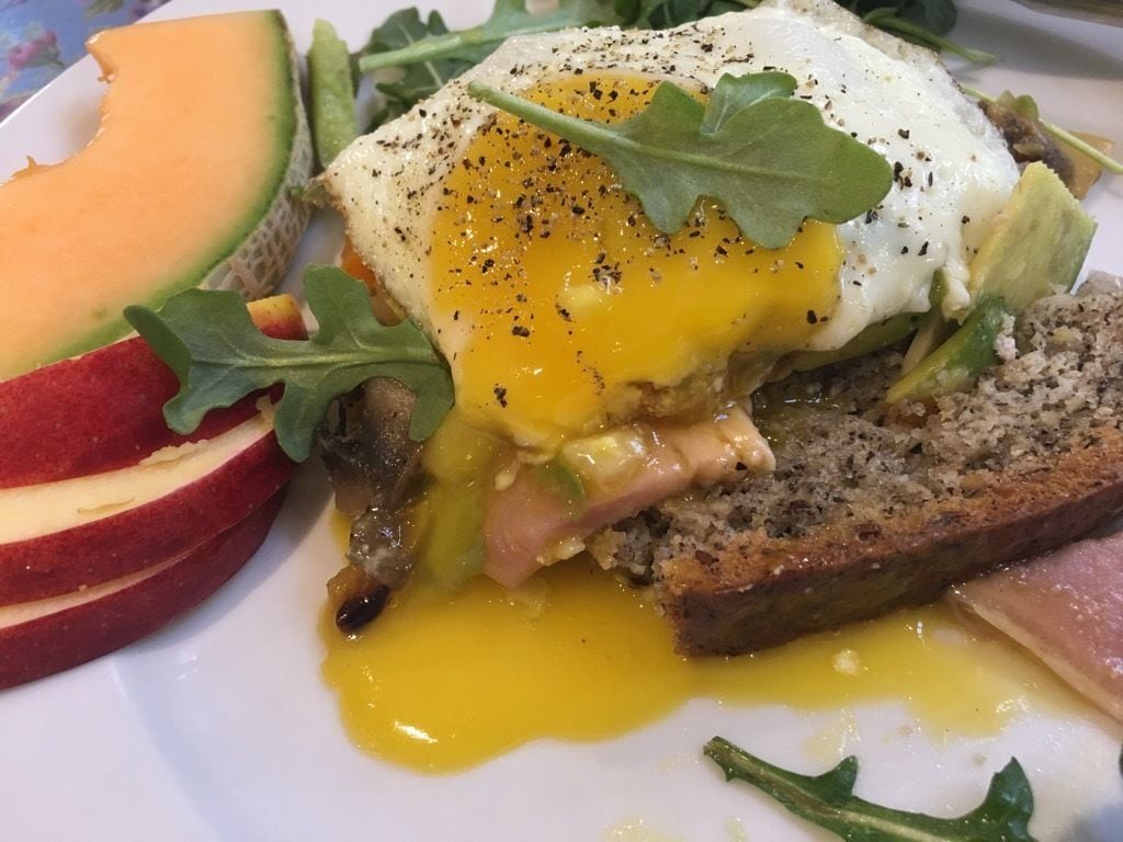 Un plato de desayuno con huevos pochados, jamón y verduras.