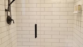 Boxe sanitário com azulejos brancos tipo metrô, chuveiro preto e maçaneta.