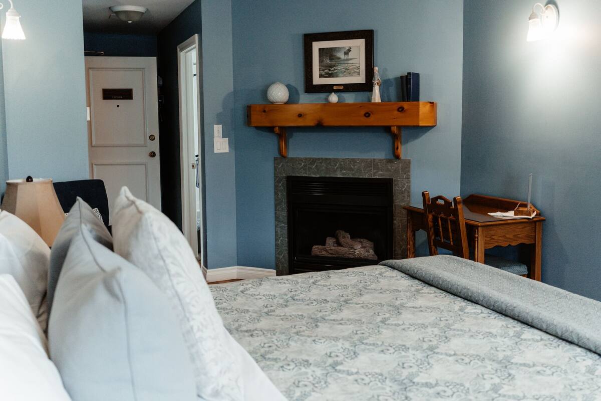 Quarto com cama, lareira, escrivaninha e cadeira.