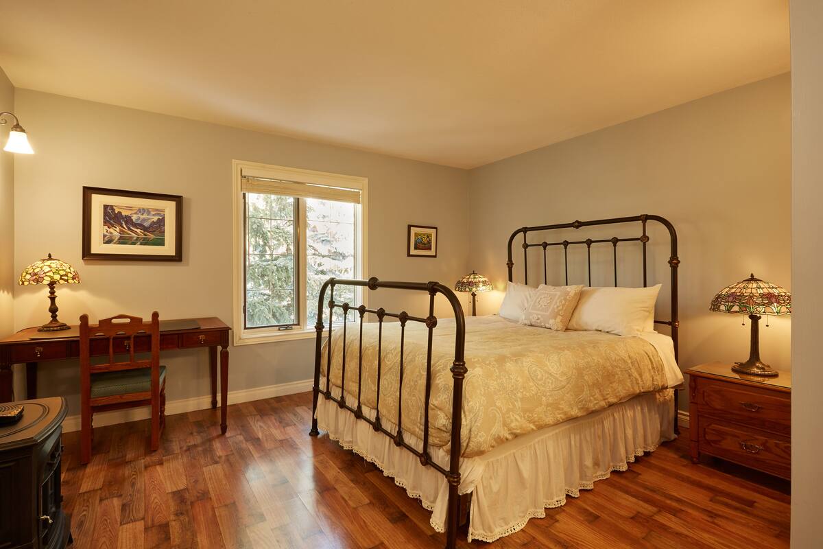 Quarto com cama de dossel, escrivaninha com cadeira, mesa de cabeceira e duas luminárias.