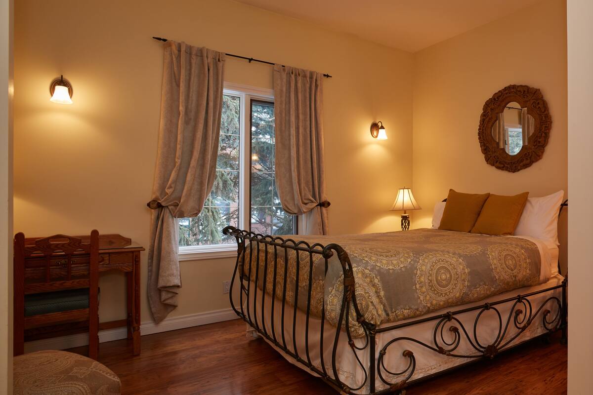 Quarto com cama, escrivaninha e janela com cortinas.