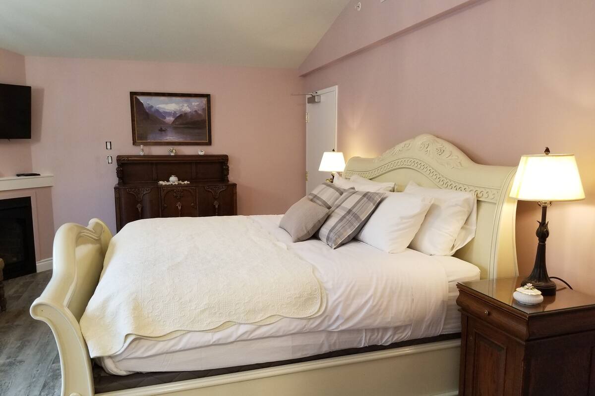 Quarto com cama, abajures, cômoda, um quadro e lareira.