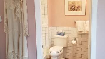 Une salle de bain avec des toilettes, un tableau encadré au mur et un vêtement suspendu.