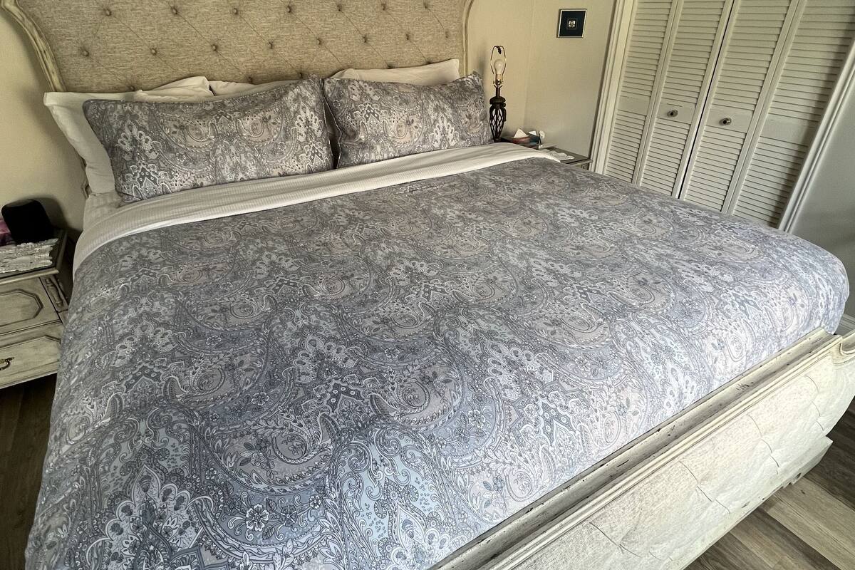 Uma cama com colcha estampada, cabeceira acolchoada e mesa de cabeceira com abajur.