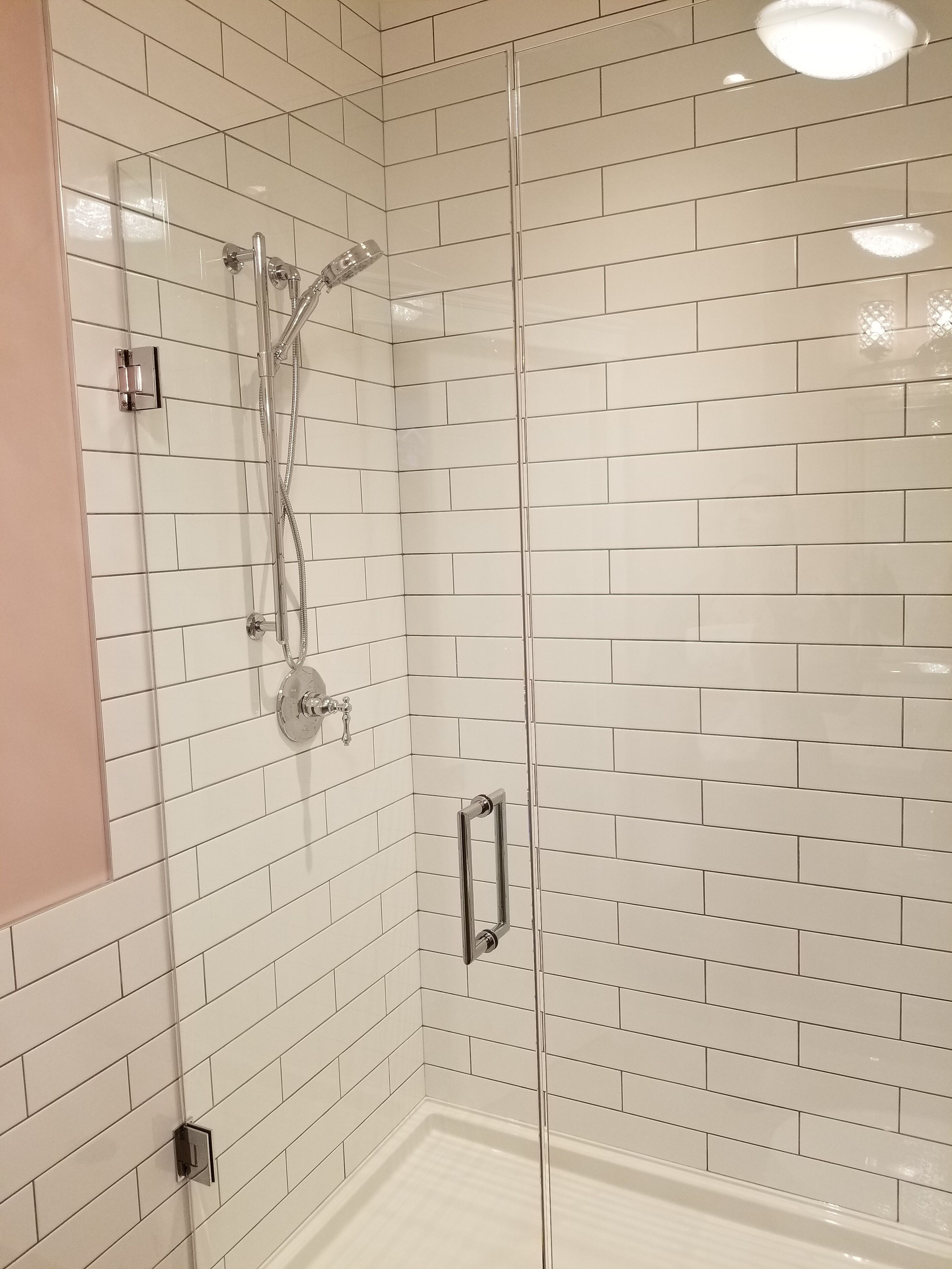 Ducha moderna con puerta de vidrio, paredes de azulejos blancos y un cabezal de ducha visible.