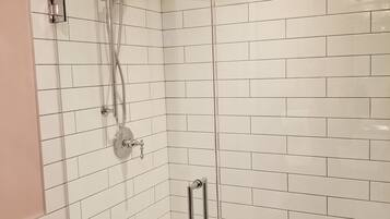 Ducha moderna con puerta de vidrio, paredes de azulejos blancos y un cabezal de ducha visible.