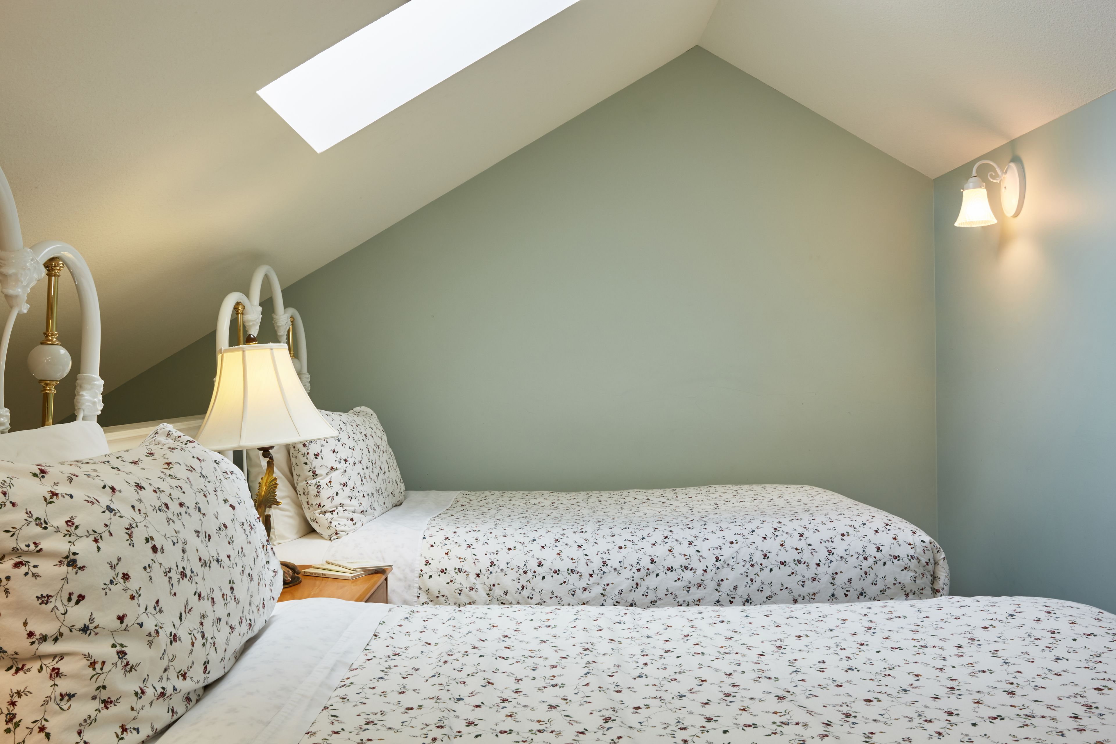 Ein Schlafzimmer mit zwei Betten, einem Oberlicht, einer Nachttischlampe und einer Wandleuchte.