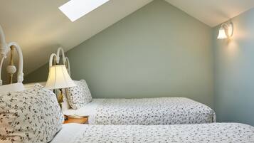 Ein Schlafzimmer mit zwei Betten, einem Oberlicht, einer Nachttischlampe und einer Wandleuchte.