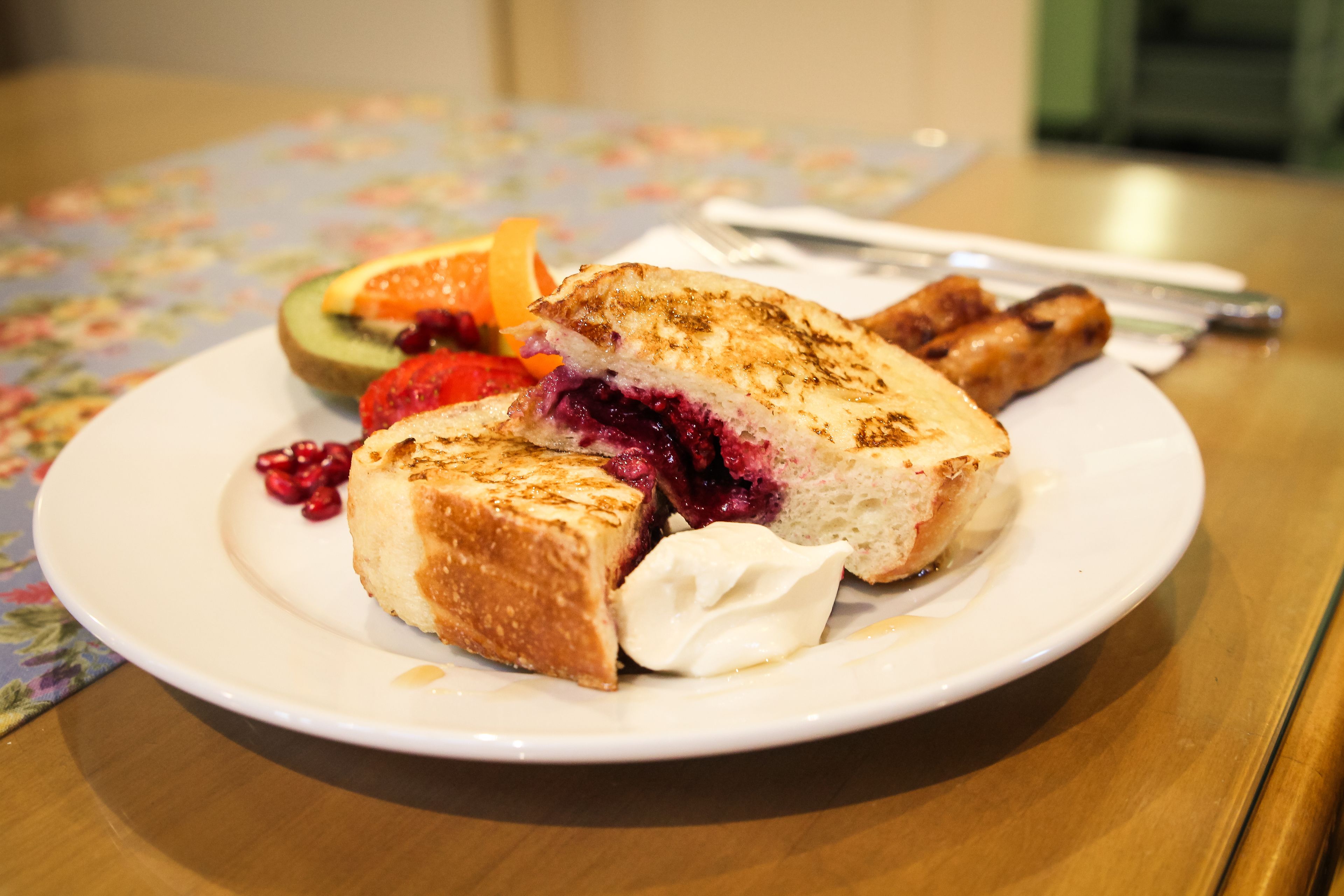 A plate with a grilled sandwich, fruit, and a pastry on a table.