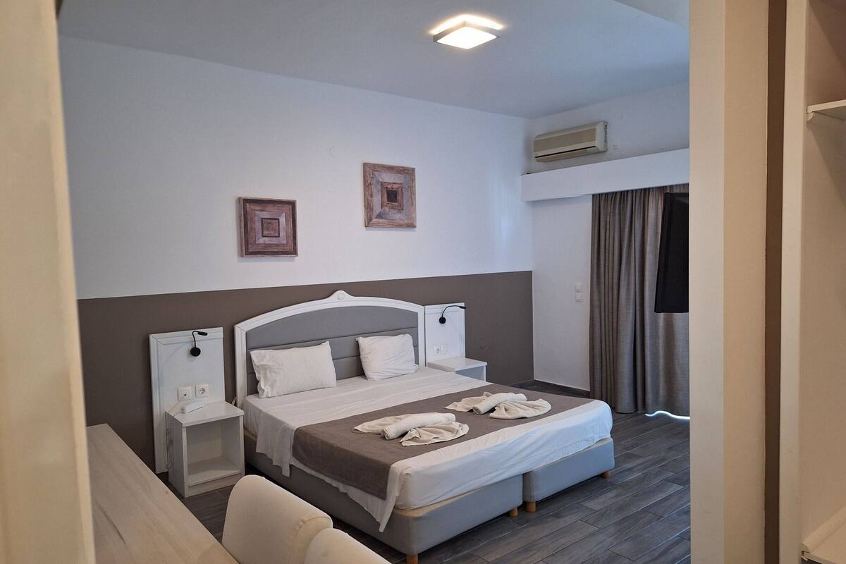 Habitación de hotel con cama, mesitas de noche, una silla, lámpara en el techo y aire acondicionado.
