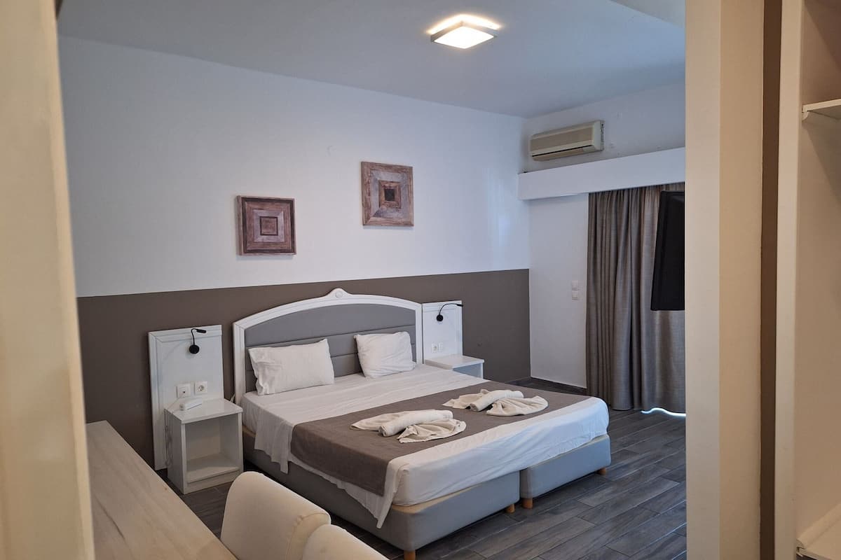 Ett hotellrum med en säng, sängbord, en stol, en taklampa och en luftkonditioneringsanläggning.