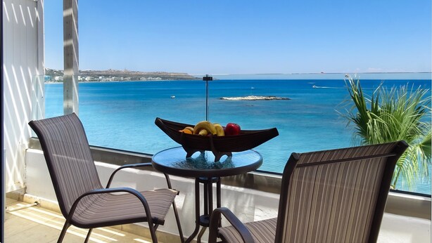A balcony with a table and chairs, overlooking a coastal view with a clear sky. - Lido Star Beach (Rhodes)