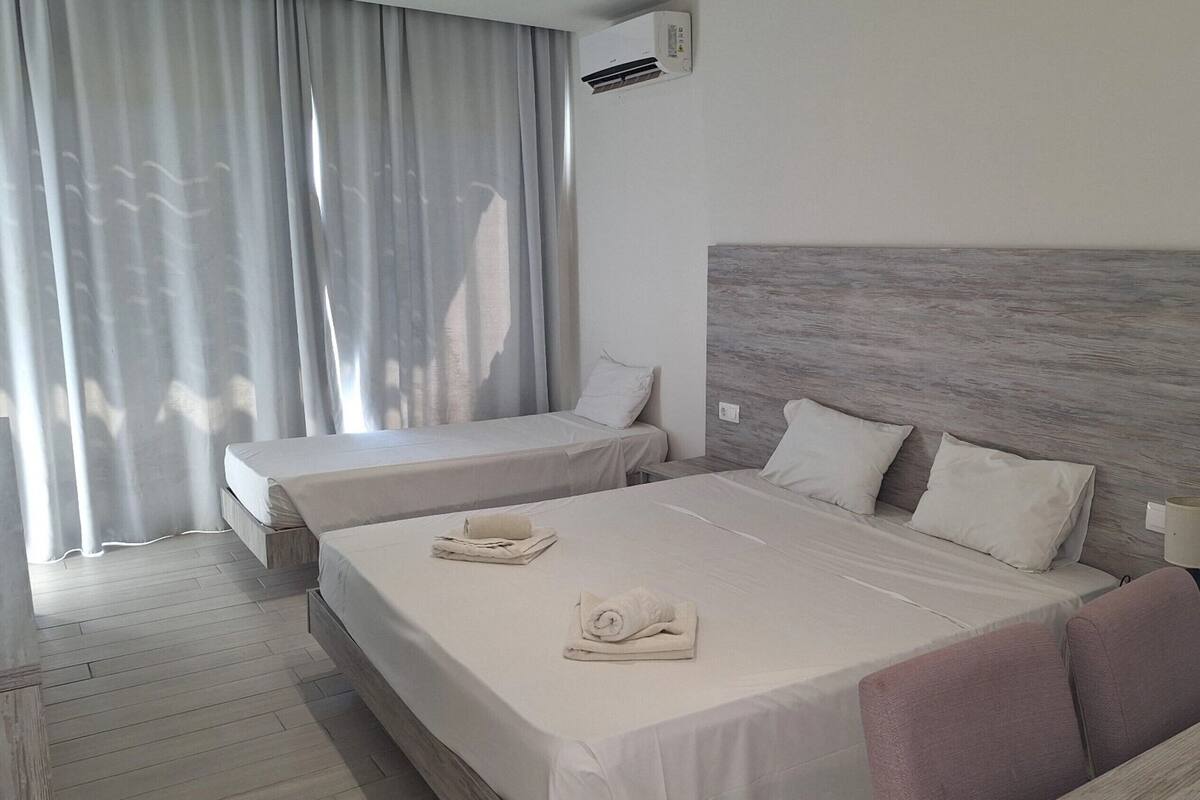 Habitación de hotel con dos camas, un cabecero grande de madera, una ventana con cortinas y un equipo de aire acondicionado.