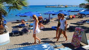 A beach with umbrellas, lounge chairs, and a signboard. - Lido Star Beach (Rhodes)