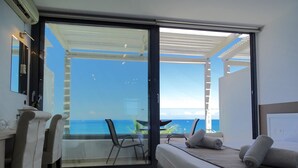 A room with a bed, a desk, and a chair, with a view of the ocean through a glass door. - Lido Star Beach (Rhodes)