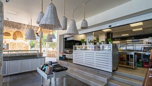 A modern kitchen with white cabinetry, hanging wicker pendant lights, and a view of the outdoor patio area. - Lido Star Beach (Rhodes)