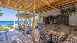 An outdoor seating area with tables and chairs, a bar, and a view of the sea. - Lido Star Beach (Rhodes)