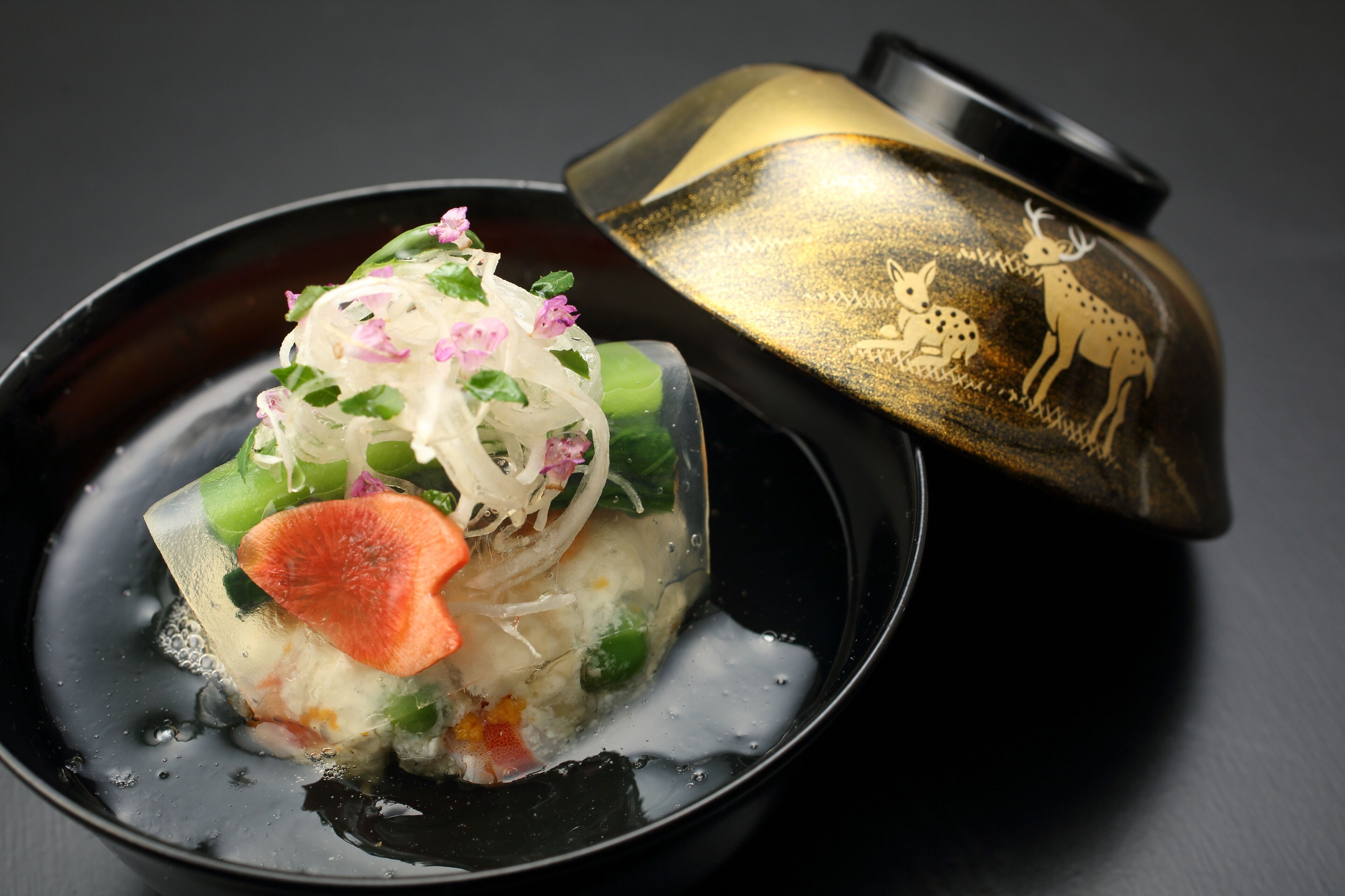 A bowl of clear soup with vegetables and a decorative lid.