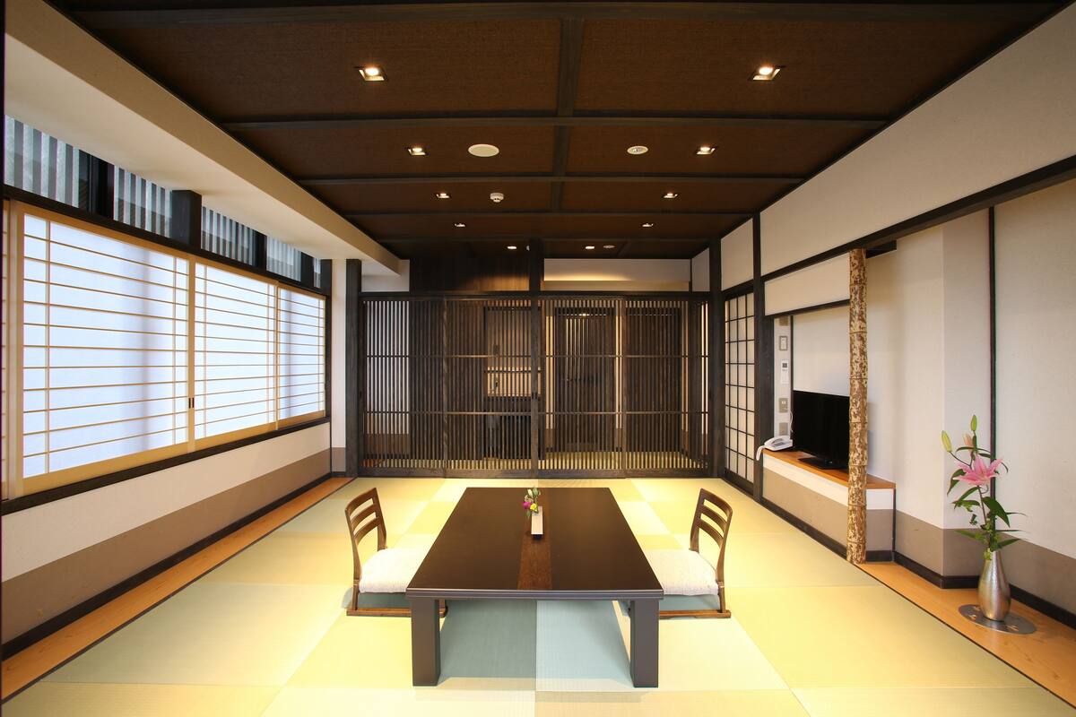 A traditional Japanese-style room with tatami flooring, a low table with cushions, sliding doors, and a television on a stand.