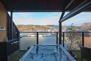 A balcony with a hot tub, a potted plant, and a view of a town and hills. - Wakasa Bettei (Nara)