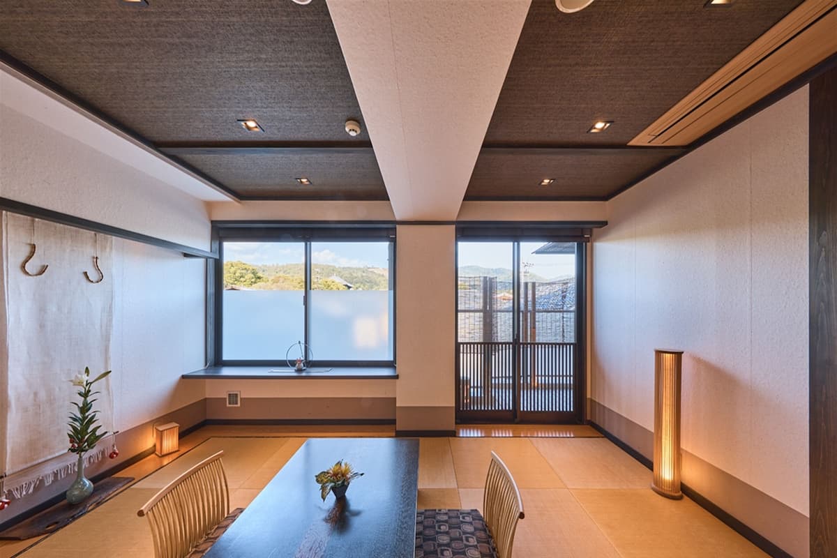 A modern interior with a large dining table, chairs, a vase with flowers, and a view of a lake through large windows.