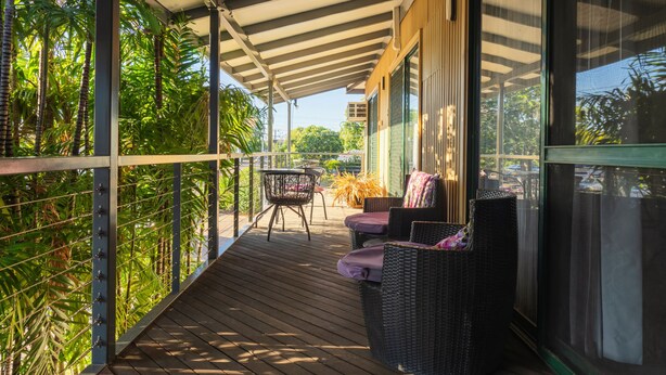 Un espacio exterior techado con terraza de madera, muebles de mimbre y vistas a la vegetación.