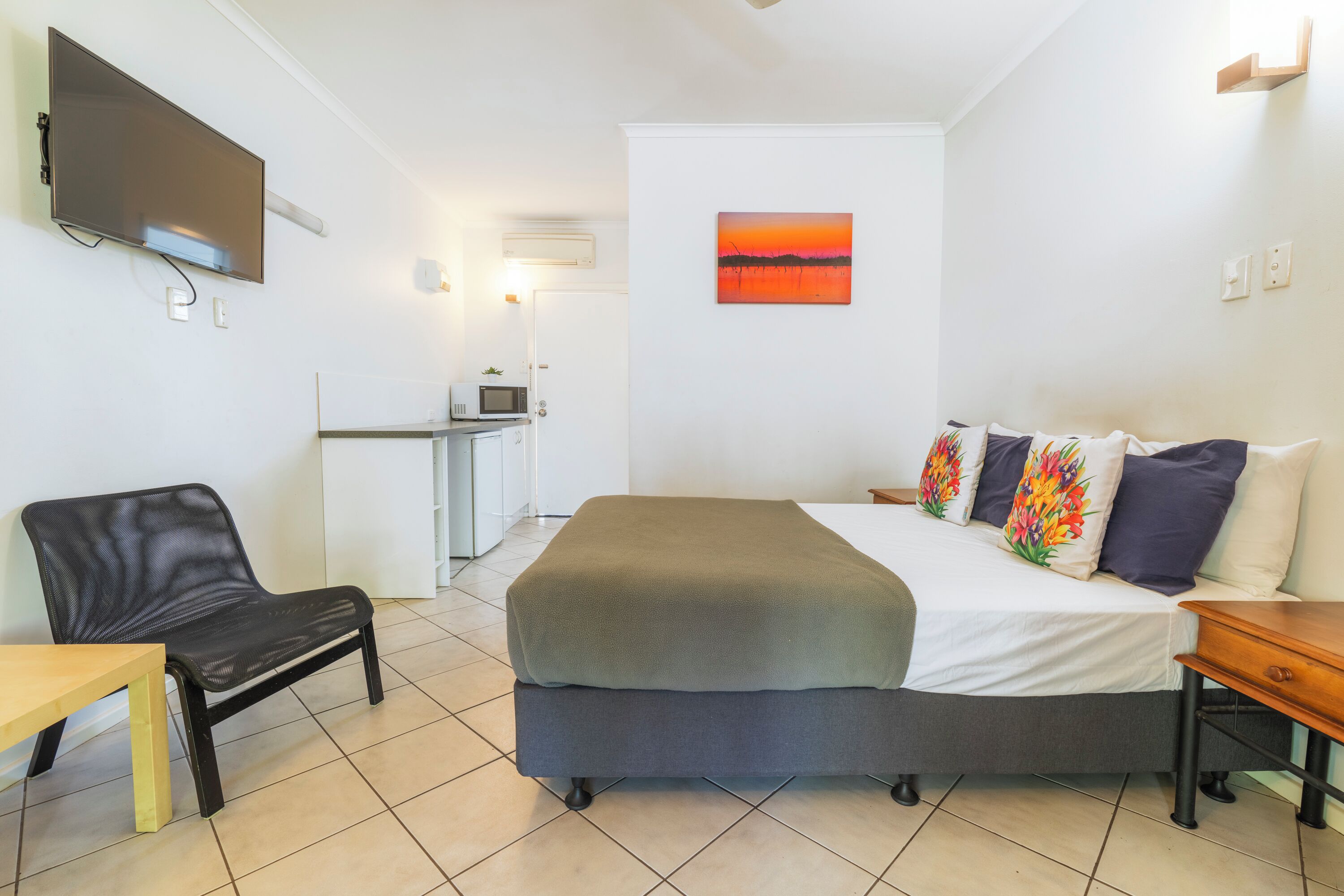 A hotel room with a bed, a desk, a chair, a TV, and a painting on the wall.