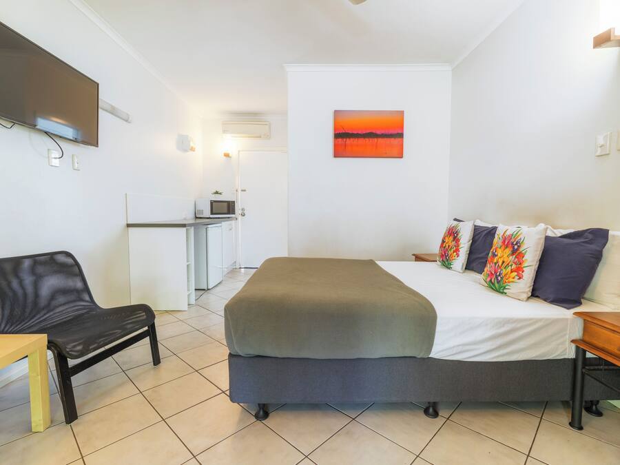A hotel room with a bed, a desk, a chair, a TV, and a painting on the wall.
