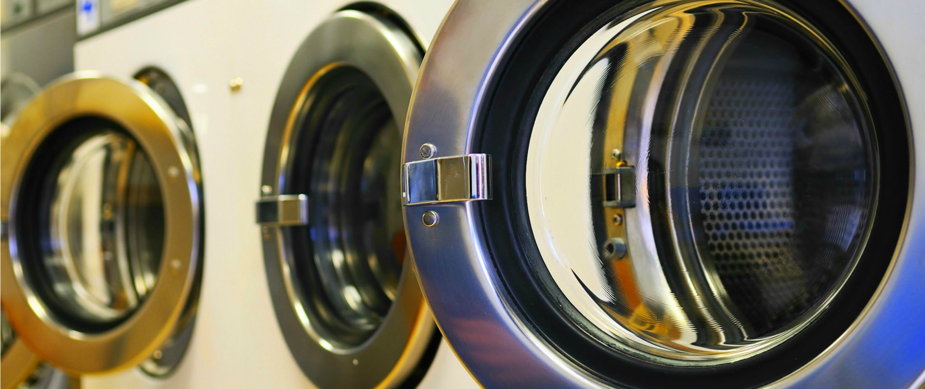 A row of front-loading washing machines with metallic and black finishes.