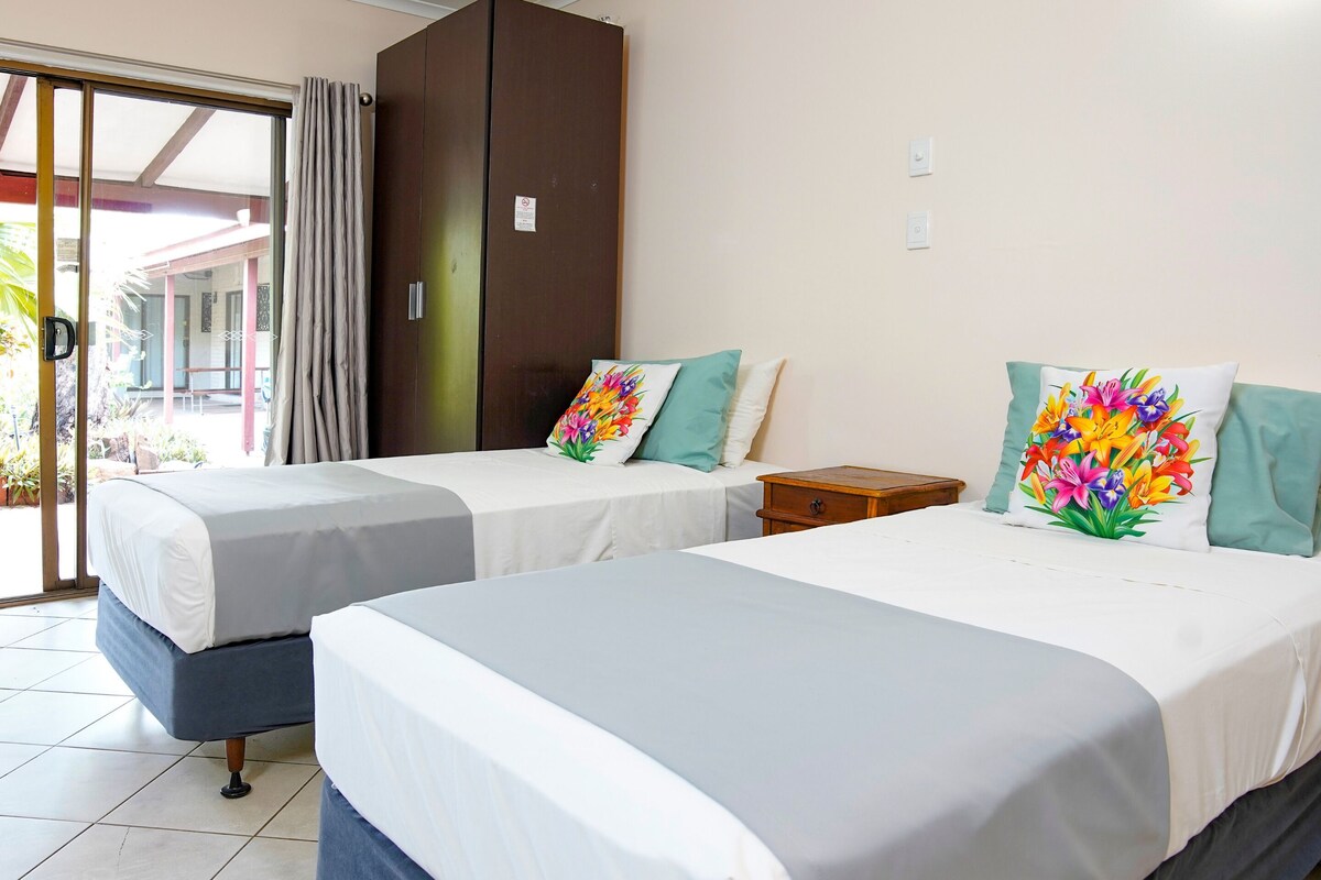 Habitación de hotel con dos camas, un armario y vistas al exterior.