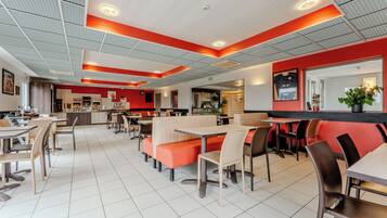 Un restaurante moderno con cabinas y mesas, un muro de acento rojo y un piso de baldosas limpias.
