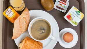 A breakfast tray with a croissant, a muffin, a cup of coffee, a glass of orange juice, a kiwi, a Nutella packet, a Valade yogurt, and a boiled egg. - ACE Hotel Arras-Beaurains (Beaurains)