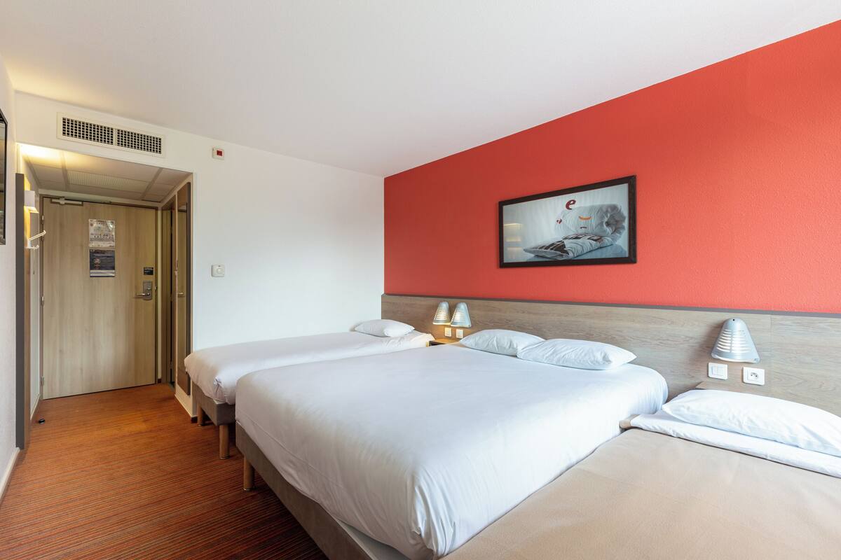 A hotel room with two beds, a red accent wall, and a framed picture above the beds.