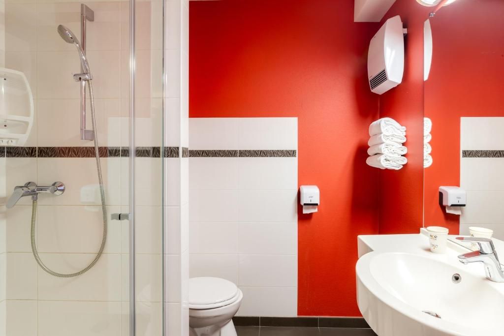 A bathroom with a glass shower enclosure, a white toilet, a sink with a mirror, and a red accent wall.