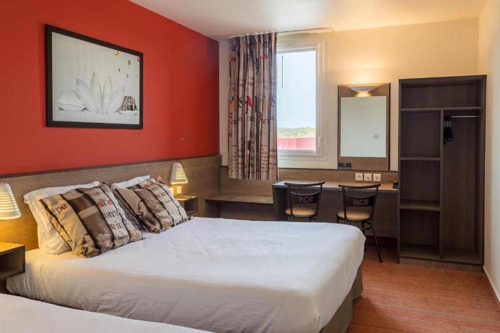 Habitación de hotel con cama, mesitas de noche, escritorio con sillas, armario, ventana con cortinas y un cuadro enmarcado en la pared.