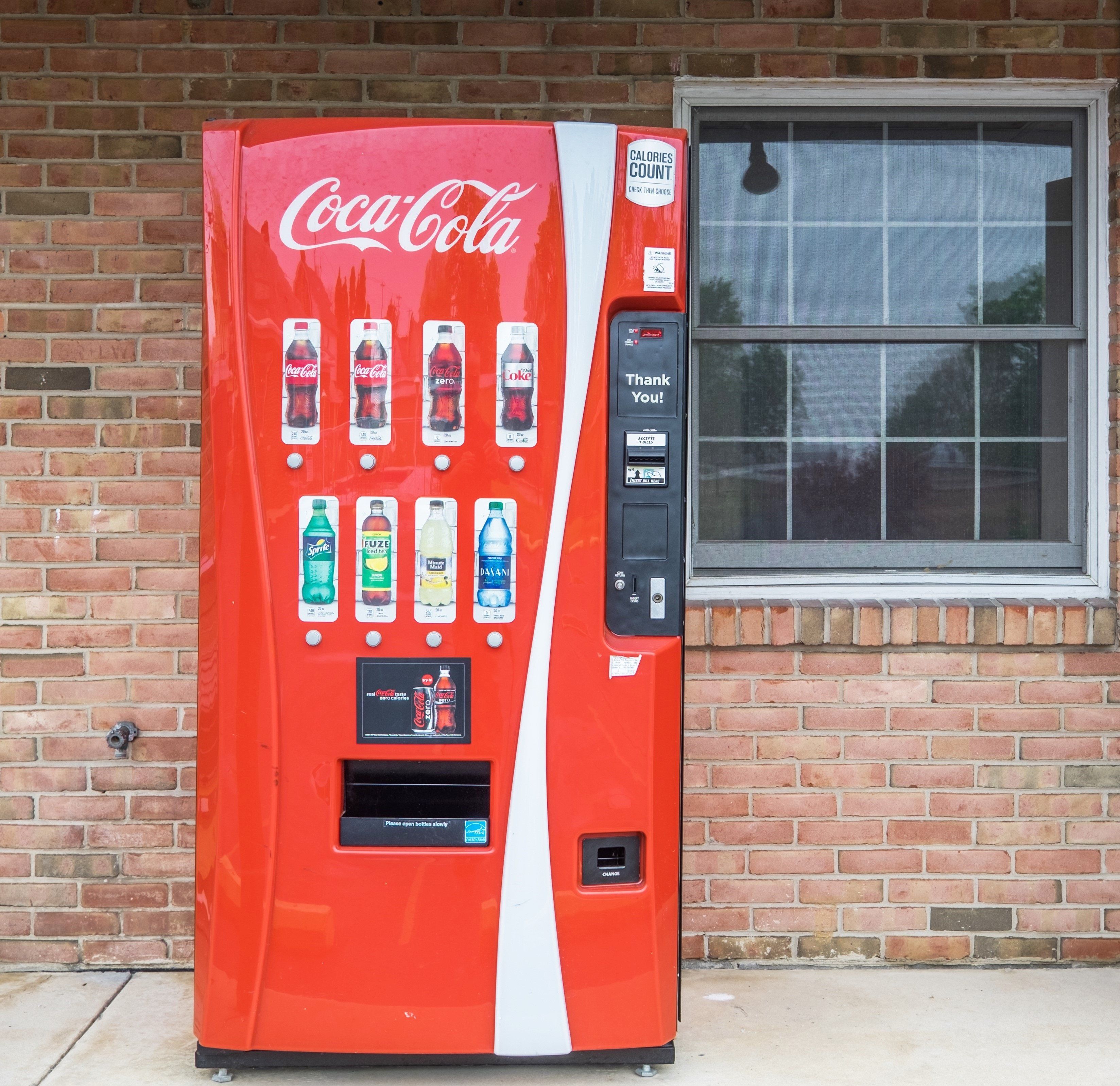 Un distributeur automatique de Coca-Cola proposant une variété de boissons et affichant le message « Merci ! ».