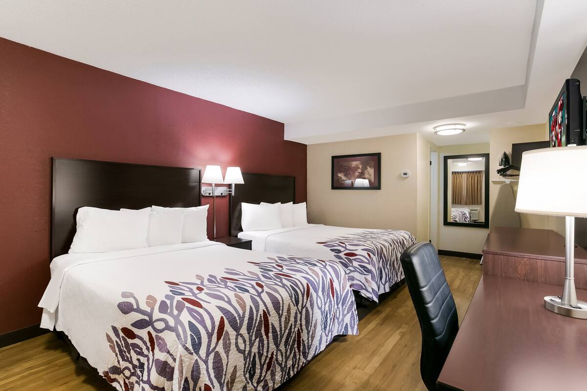 Quarto de hotel com duas camas, uma escrivaninha e uma cadeira.