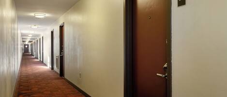 A hotel hallway with doors, a carpeted floor, and a ceiling with lights.